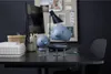 Two blue cartoon-like figures with springs in their necks are placed on a dark desk in an office setting. Produktbild-Vorschau