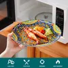 A hand holding a decorative plate with food in front of a microwave. Náhled obrázku produktu