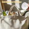 A white tote bag filled with various cosmetic items, with a hand holding a small white device above it. Voir les images du produit