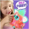 A young girl is interacting with a colorful Furby toy, which has a speech bubble above it. Náhľad obrázku produktu