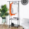A black metal clothing rack with clothes hanging on it and items on the shelves, next to a potted plant and a chair. Náhľad obrázku produktu