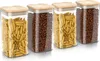 Four glass storage jars with bamboo lids, filled with pasta and coffee beans, are arranged in a row on a white background. Podgląd zdjęcia produktu