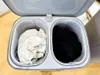 A top-down view of an open laundry hamper with two compartments, one filled with light-colored laundry and the other with dark-colored laundry. Produktbild-Vorschau