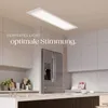 A modern kitchen with a sleek refrigerator and cabinets, illuminated by a large rectangular LED panel light. Produktbild-Vorschau