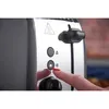 A close-up shot of a person's finger pressing a button on a gray toaster. Voir les images du produit