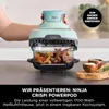 A person is holding a mint green Ninja Crispi Powerpod air fryer over a glass dish filled with food, with spices in wooden bowls nearby. Anteprima dell’immagine prodotto
