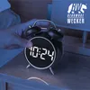 A hand is shown pressing the top of a black retro alarm clock with a white LED display showing the time 10:24. The clock is on a wooden nightstand next to a lamp. A logo for Bearware Wecker is visible in the upper right corner. Náhled obrázku produktu