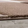 A close-up view of a rug with a geometric wave pattern, showing the texture and edge of the rug on a wooden floor. Produktbild-Vorschau