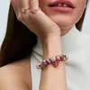 A woman's hand wearing rings and a charm bracelet, with her chin resting on her hand. Anteprima dell’immagine prodotto