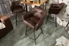 A set of brown leather bar stools are arranged around a wooden table in a loft-style setting with exposed brick walls. Produktbild-Vorschau
