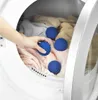 A hand places blue laundry balls into a dryer with clothes. Anteprima dell’immagine prodotto