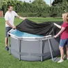 A man and a woman are covering an oval above-ground swimming pool with a black cover. Podgląd zdjęcia produktu