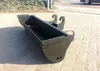 A black excavator bucket sits on a paved surface outdoors. Produktbild-Vorschau