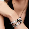 A close-up shot of a person's arms wearing two charm bracelets. Anteprima dell’immagine prodotto