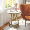 A round side table with a marble-like top and gold metal legs, placed next to a brown leather armchair near a window. Produktbild-Vorschau