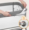 A close-up view of a baby crib with a person's hands demonstrating how to remove a washable cover. An inset image shows the cover being placed into a washing machine. Produktbild-Vorschau