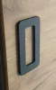 A close-up view of a dark gray handle on a wooden surface. Produktbild-Vorschau