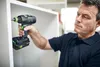 A man is using a cordless drill to assemble a white cabinet. Voir les images du produit