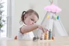 A young girl is playing with a wooden stacking toy in a brightly lit room. Produktbild-Vorschau