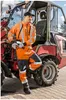 A man in high-visibility workwear stands next to a construction vehicle. Produktbild-Vorschau