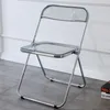 A clear, studio-like shot of a transparent folding chair with a silver metal frame, set against a white and light gray wall and a gray tiled floor.