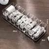 A clear acrylic organizer box filled with coiled white cables and power adapters, placed on a wooden desk. Produktbild-Vorschau