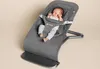 A baby is sitting in a gray Ergobaby Evolve bouncer on a light gray background. Produktbild-Vorschau