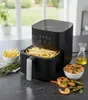 An air fryer is shown on a kitchen counter, with french fries and shrimp as food items. Produktbild-Vorschau