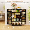 A black storage cabinet filled with various food items and kitchen supplies, set against a white wall. A table and chairs are visible to the left, and a plant to the right. Podgląd zdjęcia produktu