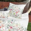 A close-up view of a floral patterned duvet cover and pillowcase set, laid out in a hammock outdoors. Produktbild-Vorschau