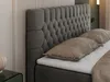 A close-up view of a dark gray upholstered headboard and pillows on a bed. Produktbild-Vorschau