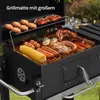 A charcoal grill with various foods cooking on it, including steaks, sausages, chicken wings, and corn on the cob. The grill is outdoors on a grassy area. Produktbild-Vorschau