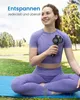 A woman is sitting on a yoga mat outdoors, holding a massage gun. Produktbild-Vorschau