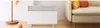 A white Xiaomi smart space heater is placed on a wooden floor next to a light-colored sofa with orange and yellow pillows. A floor lamp is visible on the left. Produktbild-Vorschau