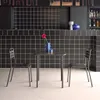 A small square table with two chairs in front of a black tiled wall. A blue vase with a red flower is on the table. Produktbild-Vorschau