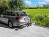 A silver station wagon with a bike rack attached to the rear, parked on a paved surface with a green field and trees in the background. Podgląd zdjęcia produktu