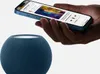 A hand holding a smartphone over a blue smart speaker. Voir les images du produit