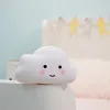 A cute cloud-shaped night light sits on the edge of a white surface, with a blurred background of a child's room. Voir les images du produit