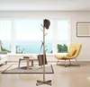 A modern living room with a large window overlooking the ocean, featuring a gold coat rack with a hat and bag, a yellow chair, and a coffee table. Produktbild-Vorschau