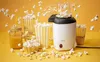 A popcorn machine is shown in action, with popcorn flying out, surrounded by popcorn cups and a drink. Podgląd zdjęcia produktu