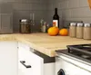 A close-up view of a kitchen countertop with a wooden surface, featuring two small pumpkins, a wine bottle, jars, and kitchen appliances. Podgląd zdjęcia produktu