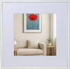 A framed picture of a red poppy hangs on a wall above a sofa in a living room. Produktbild-Vorschau