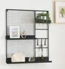 A black metal wall grid with shelves and hooks, decorated with a picture frame, a small sculpture, a plant, a purse, and a diffuser. Produktbild-Vorschau