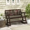 A wooden rocking garden bench sits on a patio in front of a house with shingled siding. Three framed pictures of potted plants hang on the wall behind the bench. A small side table with a vase of greenery and books sits to the left of the bench, and a pott Náhľad obrázku produktu
