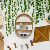 A nursery or child's room decorated with artificial ivy vines, a circular shelf with wooden blocks spelling 'BOY' and stacking toys, and a decorative kite-shaped pillow. Produktbild-Vorschau