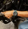 A person's hand wearing a green watch is resting on a motorcycle handlebar. Produktbild-Vorschau
