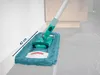 A mop with a teal cleaning pad is shown cleaning along a white baseboard on a gray tiled floor. Produktbild-Vorschau