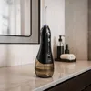 A black and brown water flosser sits on a marble countertop in a bathroom, with a mirror and soap dispenser in the background. Náhľad obrázku produktu