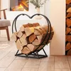A heart-shaped log holder filled with firewood next to a fireplace. Produktbild-Vorschau