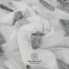 A close-up shot of white fabric with a gray feather pattern, showing the texture and detail of the material. Produktbild-Vorschau